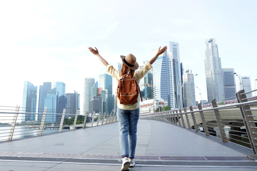 Solo young woman traveler with a backpack and hat exploring downtown Singapore, surrounded by modern architecture and vibrant city life