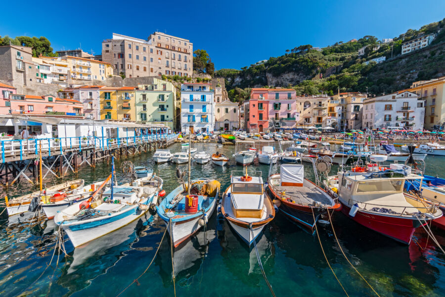 Small fishing boats docked at Marina Grande in Sorrento, Italy, with the scenic Amalfi Coast in the background