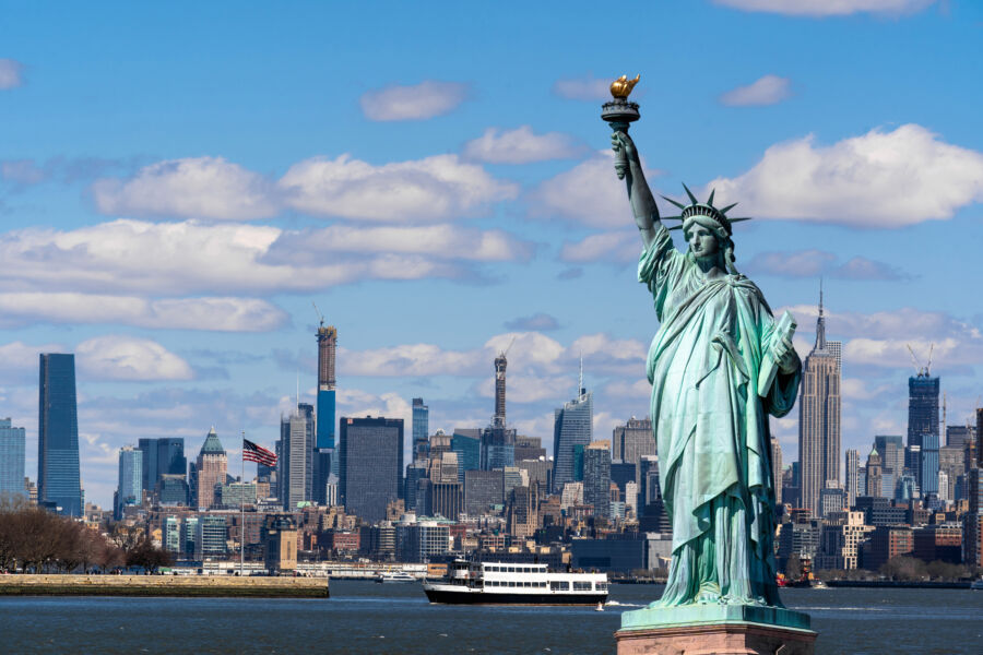 The Statue of Liberty towers above the Lower Manhattan riverside, framed by the iconic New York City skyline