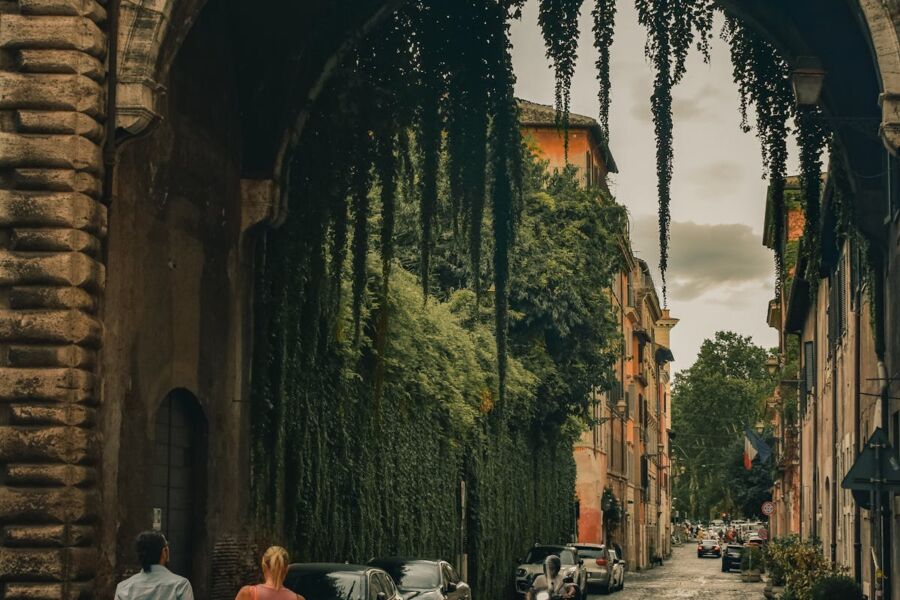 Charming historic street with cobblestones, archway, greenery, and people enjoying a leisurely walk.