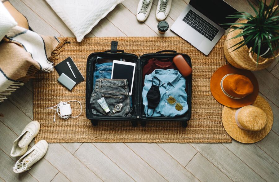 Top view of a suitcase being packed for a vacation, showcasing travel essentials in the new normal