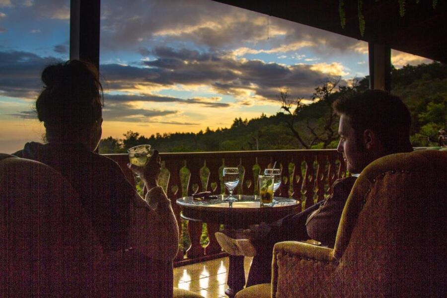 Couple relaxes on a porch at sunset, enjoying drinks and natures serene beauty.