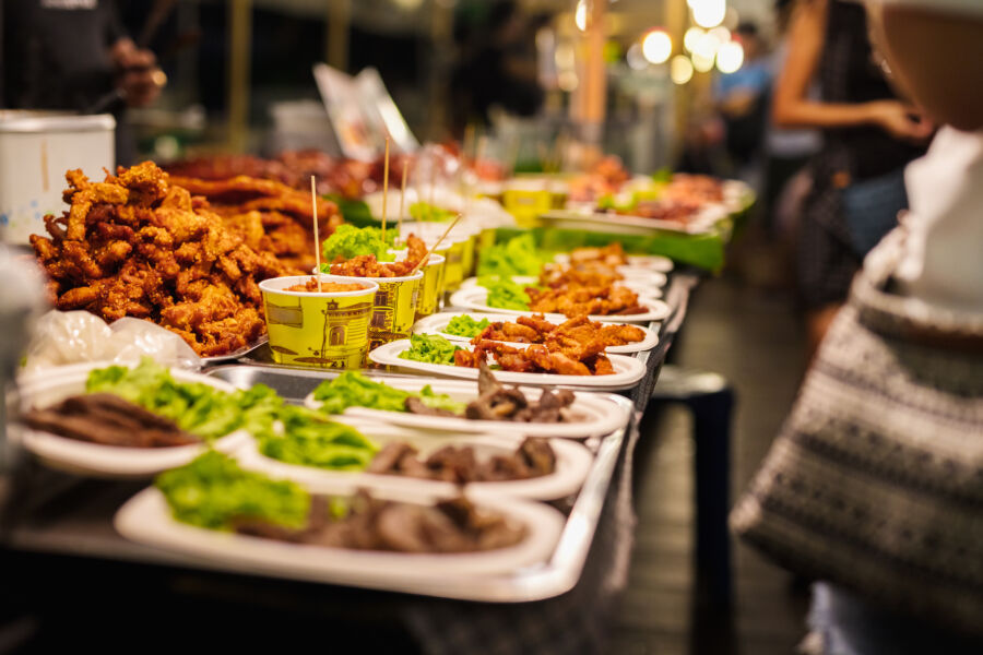 Lively street food stall in a Thai market, showcasing golden fried chicken and a variety of local delicacies