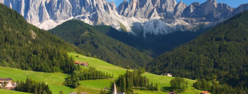 Scenic view of the Dolomites in the European Alps, characterized by towering peaks and vibrant green valleys beneath a bright sky