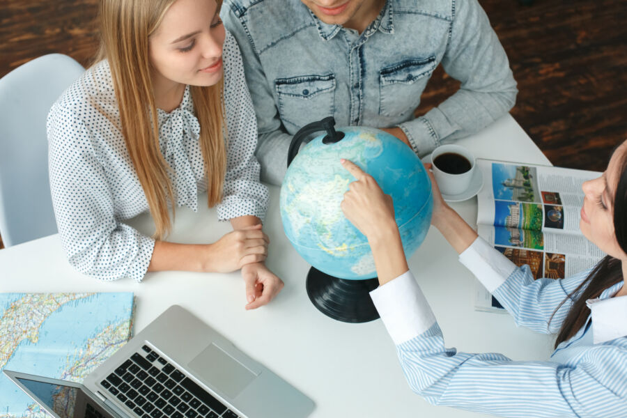 Young couple discussing travel plans with a travel agent, exploring destinations on a globe in a tour agency setting