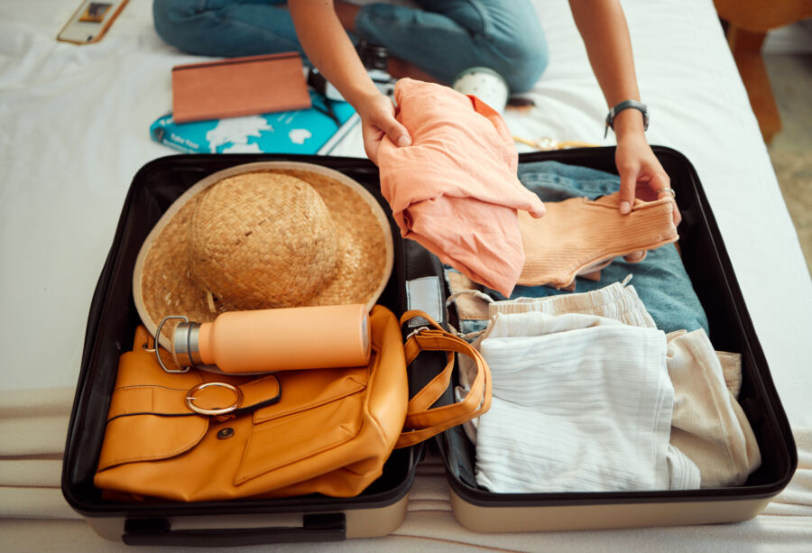 Woman organizes her suitcase on a bed, ready for summer vacation and adventure, surrounded by clothing items