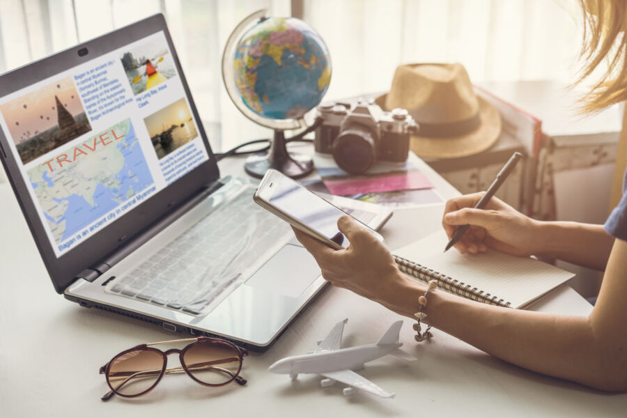 Young woman sits at a table, surrounded by travel guides and a laptop, enthusiastically planning her next trip