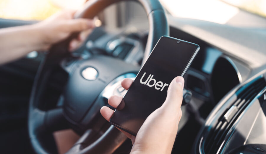 Uber driver inside a vehicle, showing a smartphone with the Uber app open