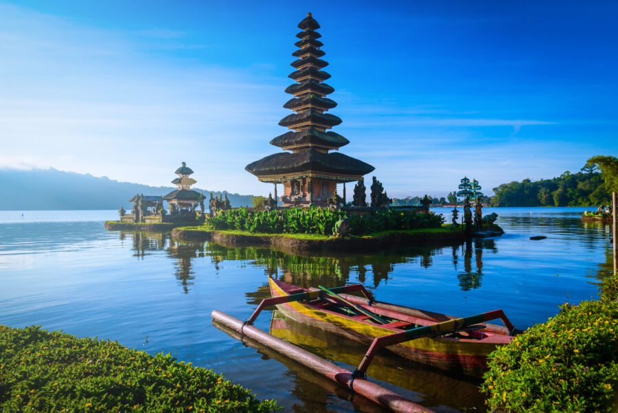 Sunrise over Ulun Danu Beratan Temple, featuring a boat on Bratan Lake, highlighting Bali's stunning natural beauty