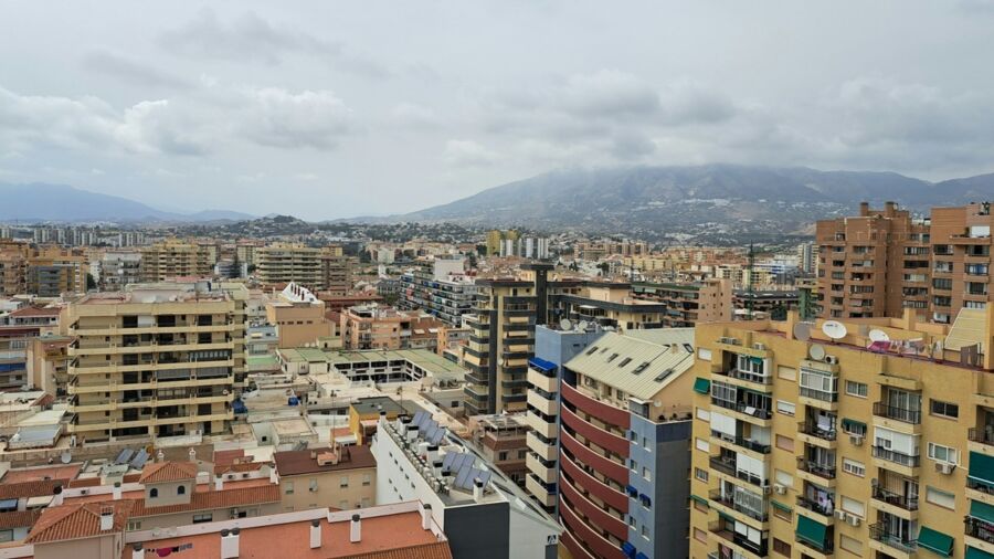 Sprawling urban landscape with diverse architecture against mountainous backdrop under overcast skies.