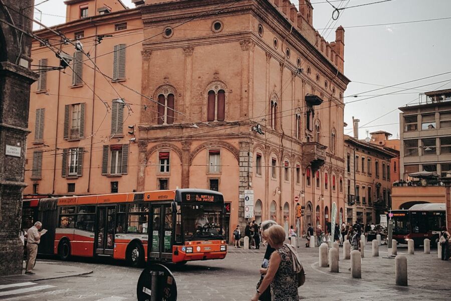 European city street scene with vintage architecture, orange and white bus, and bustling pedestrians.