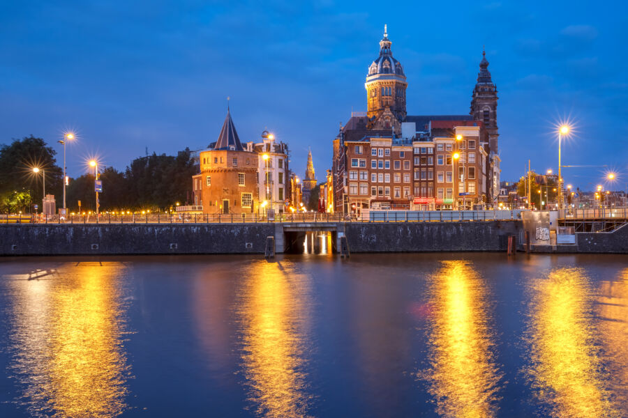 Night view of Weeping Tower next to the Basilica of Saint Nicholas, reflecting on the Amsterdam canal's serene waters