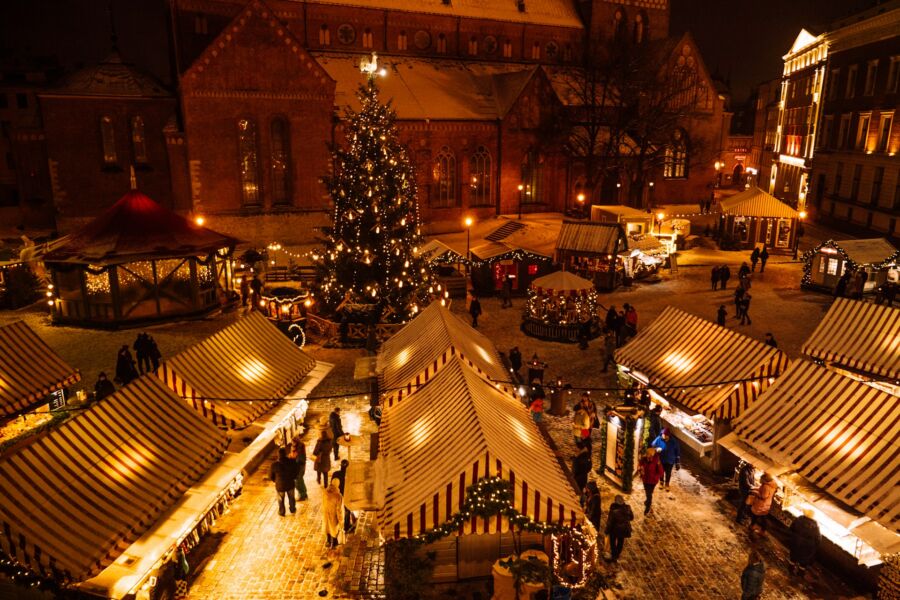 Munich Christmas market at night with illuminated tree, stalls, festive decorations, and visitors.