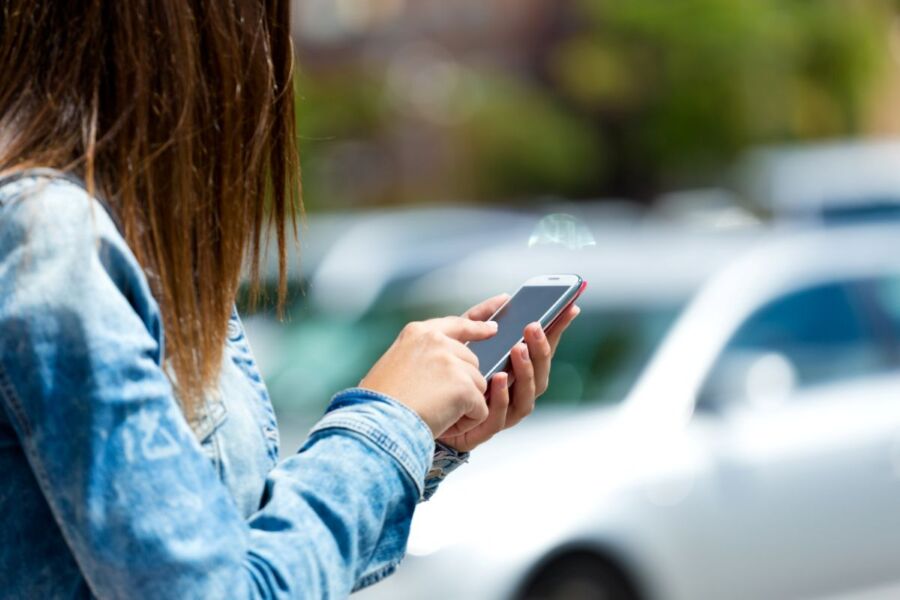 Young person using smartphone outdoors on a sunny day in urban setting.