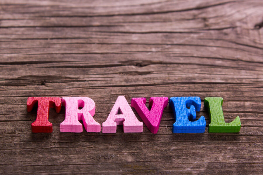 Colorful wooden letters spelling "travel" arranged on a weathered wooden table