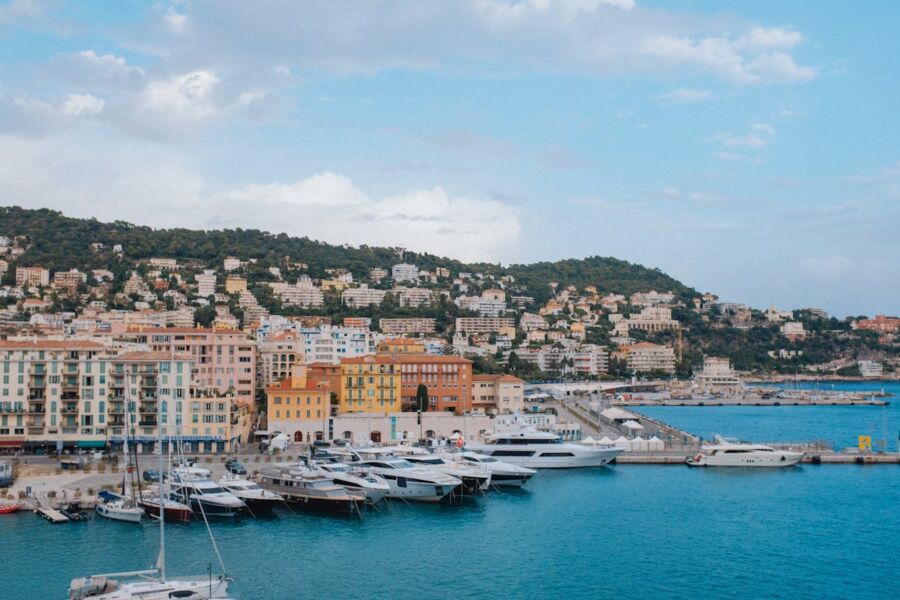 Luxurious Mediterranean yachts docked in turquoise marina with colorful seaside architecture.