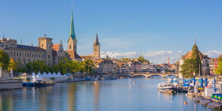 Picturesque Zurich waterfront view with calm river, historical architecture, and inviting outdoor market.